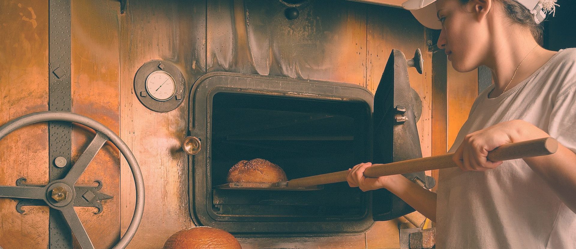 Eine Bäckerin holt ein Brot aus dem Holzofen